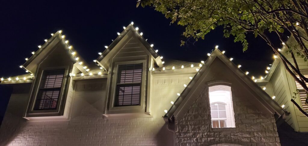 Two-story house at night with warm string lights along the peaked rooflines.